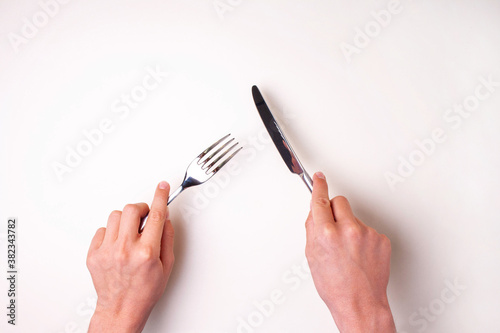 Hands hold a knife with a fork on a white table isolated. View from above