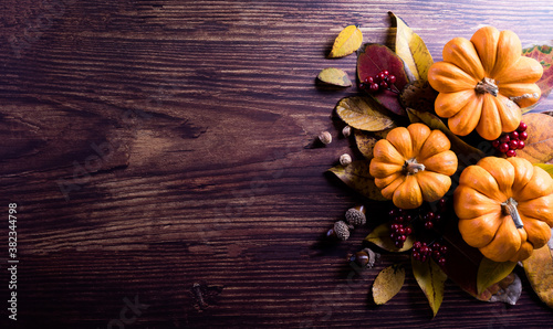 Thanksgiving background decoration from dry leaves and pumpkin on dark wooden background. Flat lay, top view with copy space.