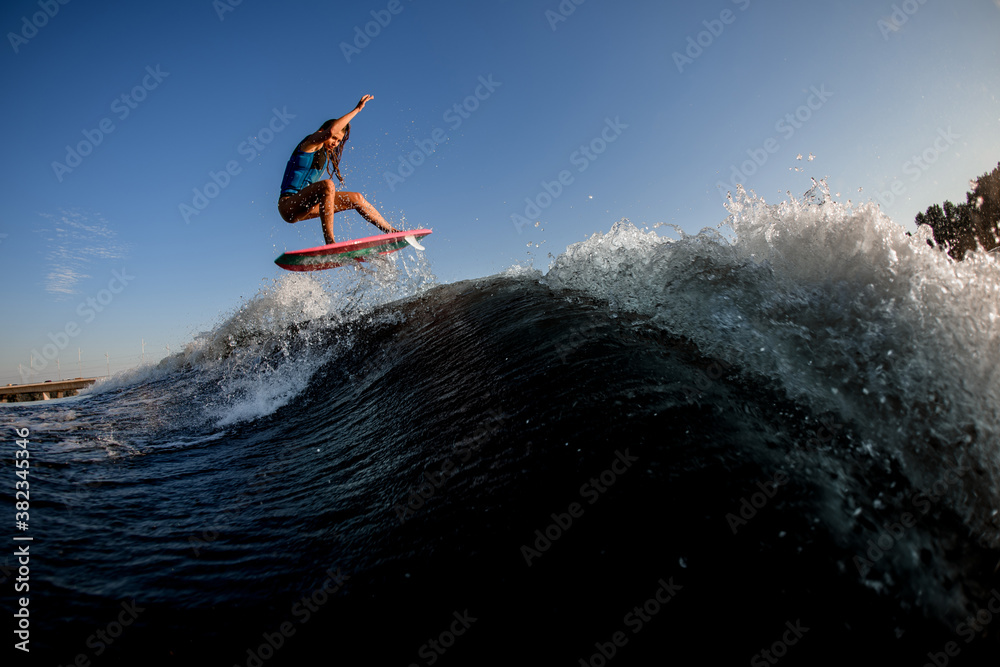 active athletic woman jumping over big splashing wave on surf style wakeboard.