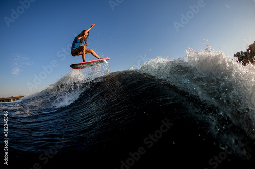 active athletic woman jumping over big splashing wave on surf style wakeboard. © fesenko