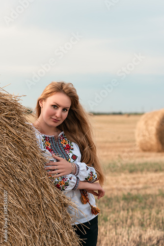 Beautiful ukrainian young woman in a field with wheat bales in embroidered shirt