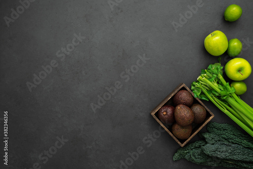 Top view of kale, celery, apples, limes and wooden box with avocados on the black background with copy space. Ingredients for healthy breakfast.
