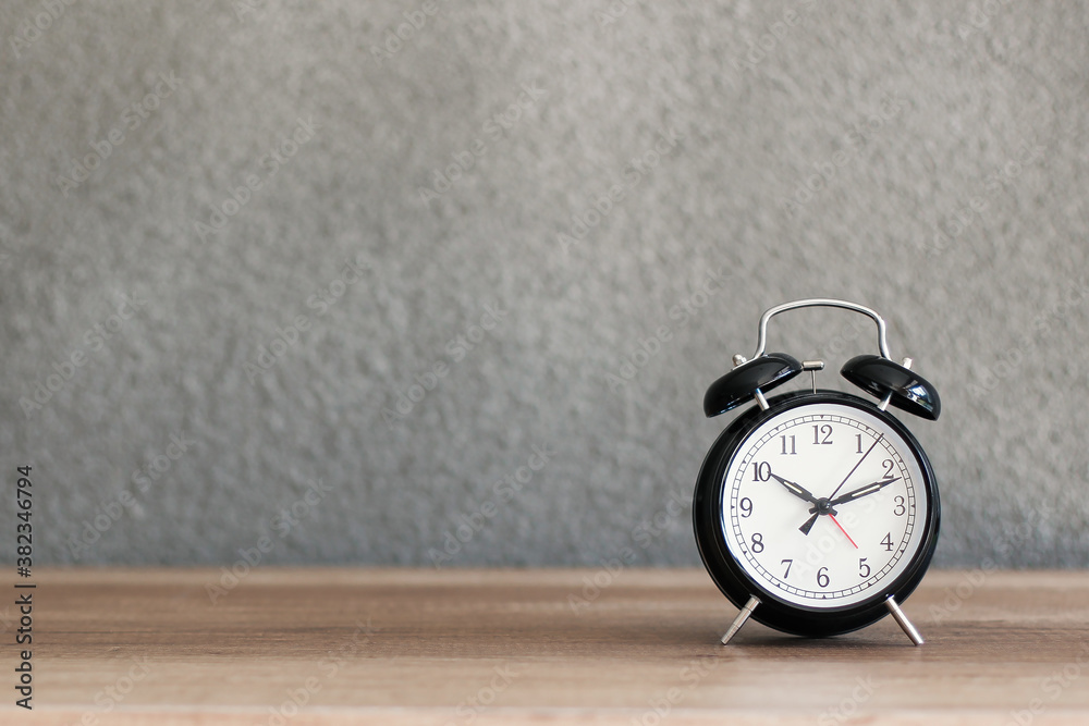 Black metal retro alarm clock on wooden desk with concrete wall on the background Black metal retro alarm clock on wooden desk with concrete wall on the background