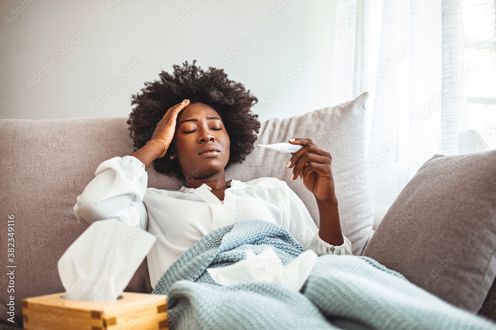 Woman with flu in bed, she use home medicine to handle sickness. Sickness, seasonal virus problem concept. Woman being sick having flu lying on sofa looking at temperature on thermometer. Woman with flu in bed, she use home medicine to handle sickness. Sickness, seasonal virus problem concept. Woman being sick having flu lying on sofa looking at temperature on thermometer.