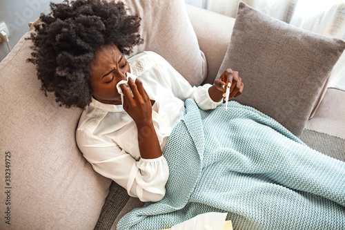 Cold And Flu. Portrait Of Ill African AmericanWoman Caught Cold, Feeling Sick And Sneezing In Paper Wipe. Closeup Of Beautiful Unhealthy Girl Covered In Blanket Wiping Nose. Healthcare Concept. photo