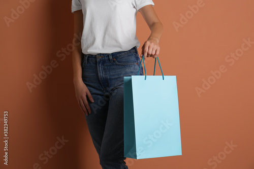 Woman with paper shopping bag on light brown background, closeup