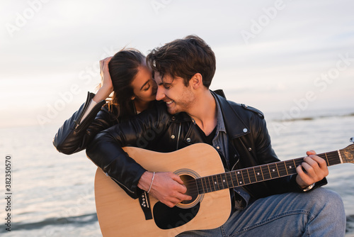 Young woman kissing boyfriend playing acoustic guitar near sea at sunset © LIGHTFIELD STUDIOS