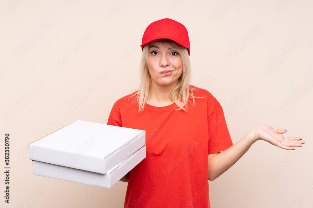 Pizza delivery Russian woman holding a pizza over isolated wall making doubts gesture while lifting the shoulders Pizza delivery Russian woman holding a pizza over isolated wall making doubts gesture while lifting the shoulders