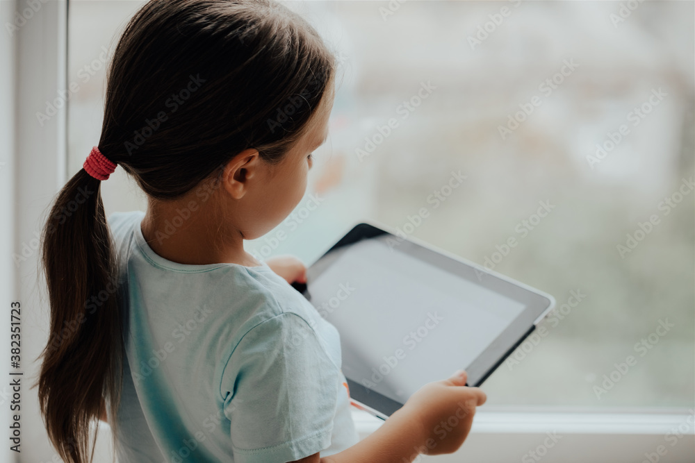 European Little Girl with Tablet pc Relaxing in a spacious room near the Window European Little Girl with Tablet pc Relaxing in a spacious room near the Window