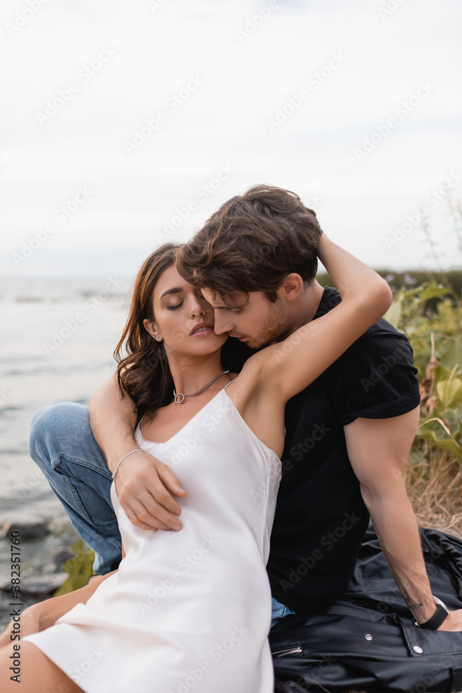 Woman in dress hugging boyfriend on leather jacket on beach