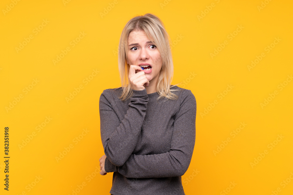 Young blonde woman over isolated yellow background nervous and scared Young blonde woman over isolated yellow background nervous and scared