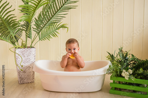 surprised baby sitting in the bath and eating an orange on a wooden background