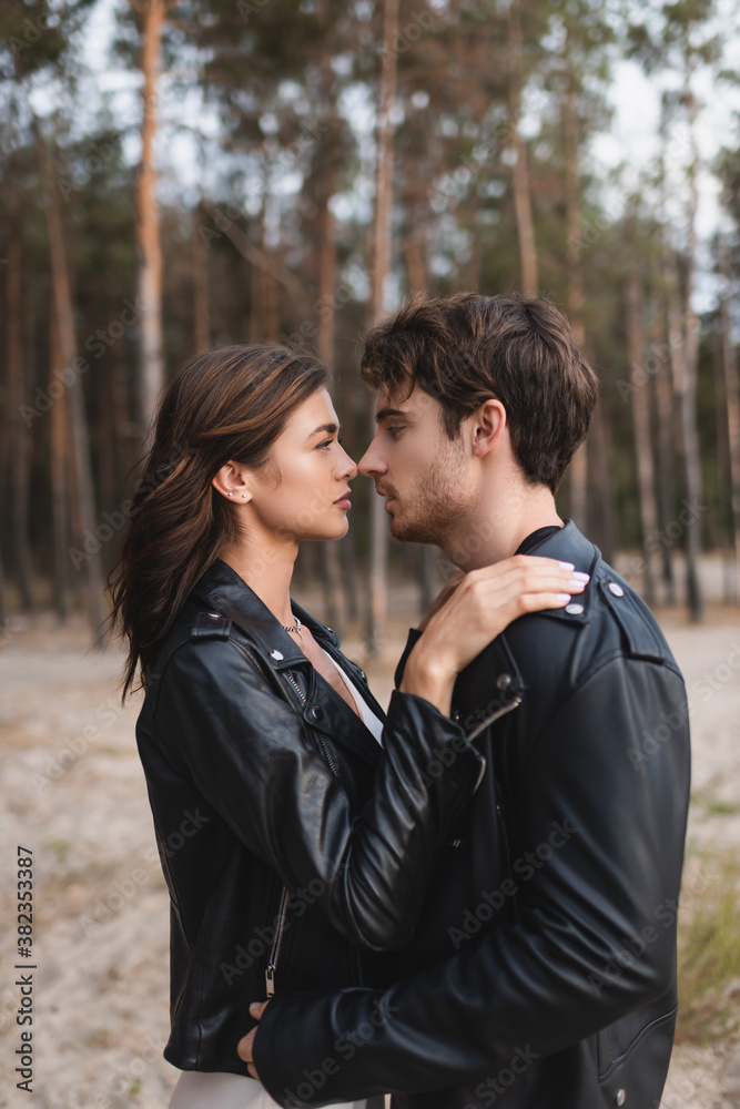 Side view of brunette woman in leather jacket embracing boyfriend in forest Side view of brunette woman in leather jacket embracing boyfriend in forest
