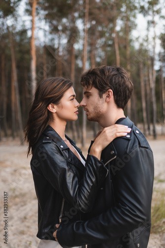 Side view of brunette woman in leather jacket embracing boyfriend in forest