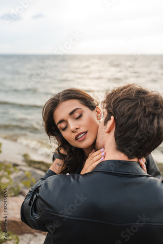 Man in black leather jacket kissing girlfriend in neck near sea on beach © LIGHTFIELD STUDIOS