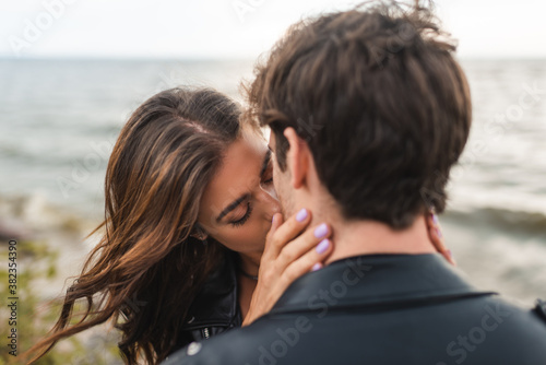 Selective focus of young woman kissing boyfriend on sea coast