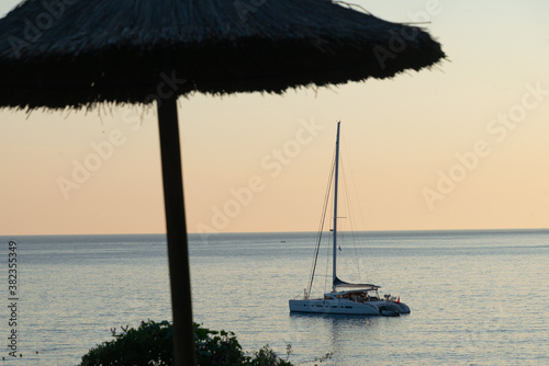 Yacht catamaran sailboat on sea with beach straw umbrella sunset