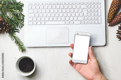 Hands typing white laptop. Christmas decoration pine branches and pinecones and tea cup