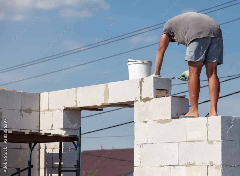 A worker builds the walls of a house from aerated concrete bricks. A worker builds the walls of a house from aerated concrete bricks.