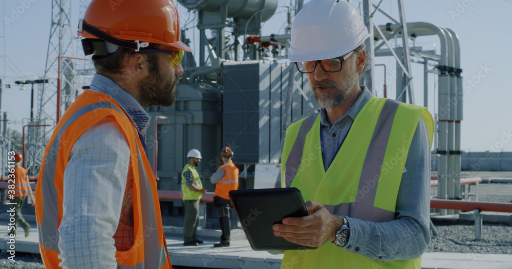 Engineers in masks using tablet on power station Engineers in masks using tablet on power station