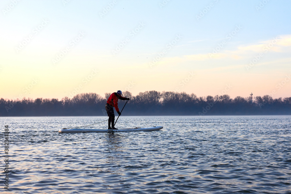 Water tourists is paddling on SUP (Stand up paddle board) at Danube river at cold season. Concept of water tourism, healthy lifestyle and recreation at winter