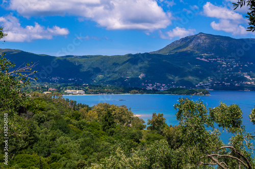 Beautiful summer landscape with sea bay with calm water, village and mountains on the horizon and clouds on blue sky.