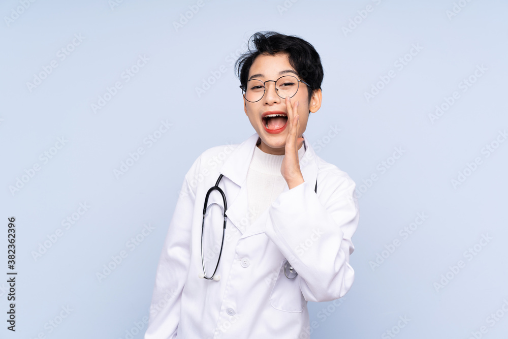 Doctor Asian woman over isolated blue background shouting with mouth wide open Doctor Asian woman over isolated blue background shouting with mouth wide open