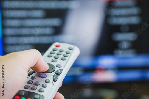 white remote control in a man's hand against the background of a blurred TV screen