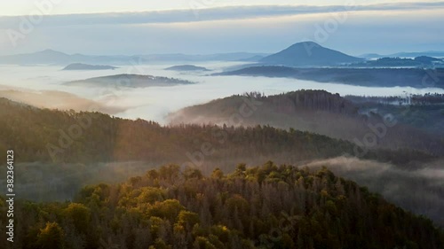 Daybreak moments in hilly landscape during fall season. Thick fog is flowwing from hill to Labe river valely. Czech Switzerland national park.
