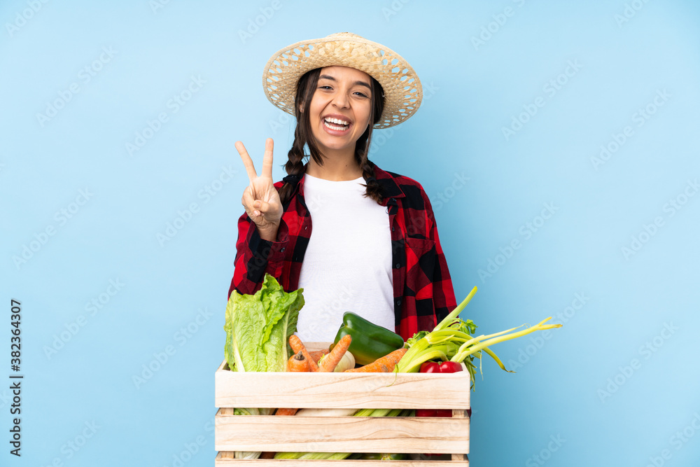 Young farmer Woman holding fresh vegetables in a wooden basket smiling and showing victory sign