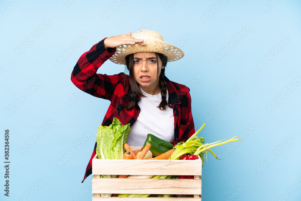 Young farmer Woman holding fresh vegetables in a wooden basket looking far away with hand to look something