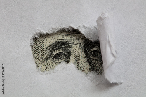 Benjamin Franklin macro peeking through torn white paper photo