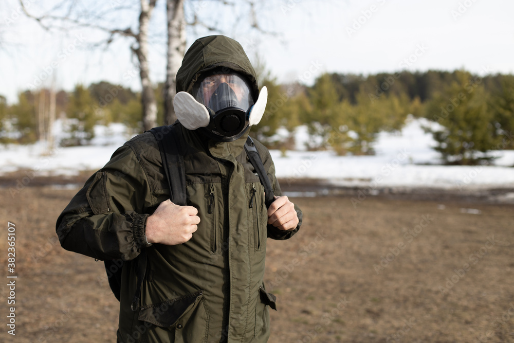 a man with a backpack and in a gas mask against the background of a spring forest