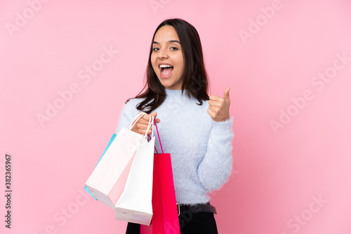 Young woman with shopping bag over isolated pink background showing ok sign and thumb up gesture