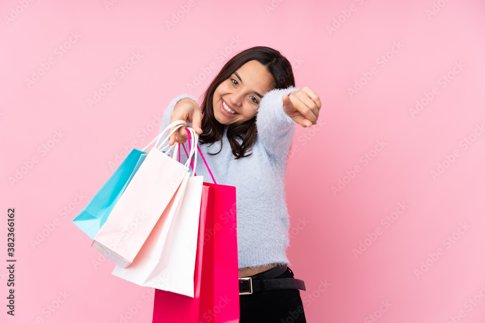 Young woman with shopping bag over isolated pink background points finger at you while smiling