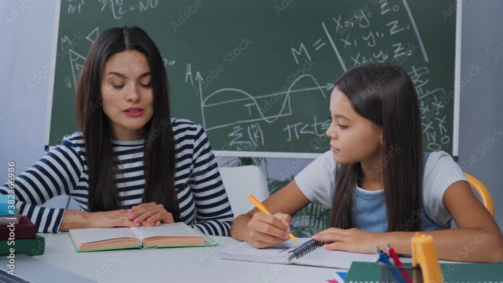 mother reading book while doing homework with schoolgirl mother reading book while doing homework with schoolgirl