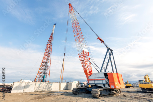 The big crawler crane and other construction machineries are working to build pier of the harbor. A crawler crane has its boom mounted on an undercarriage fitted with a set of crawler tracks.