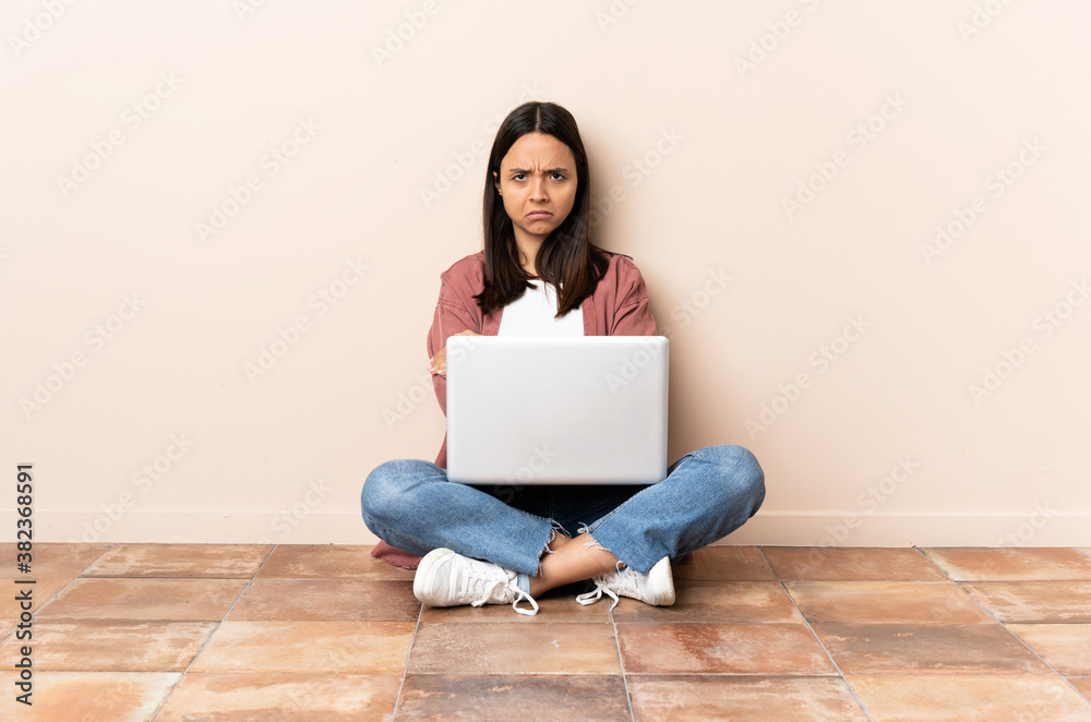 Young mixed race woman with a laptop sitting on the floor with unhappy expression Young mixed race woman with a laptop sitting on the floor with unhappy expression