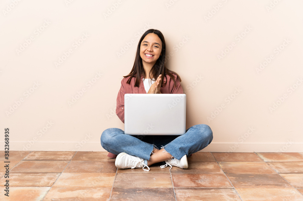 Young mixed race woman with a laptop sitting on the floor applauding after presentation in a conference Young mixed race woman with a laptop sitting on the floor applauding after presentation in a conference