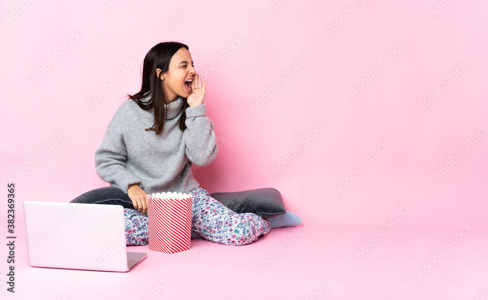 Young mixed race woman eating popcorn while watching a movie on the laptop shouting with mouth wide open to the side Young mixed race woman eating popcorn while watching a movie on the laptop shouting with mouth wide open to the side