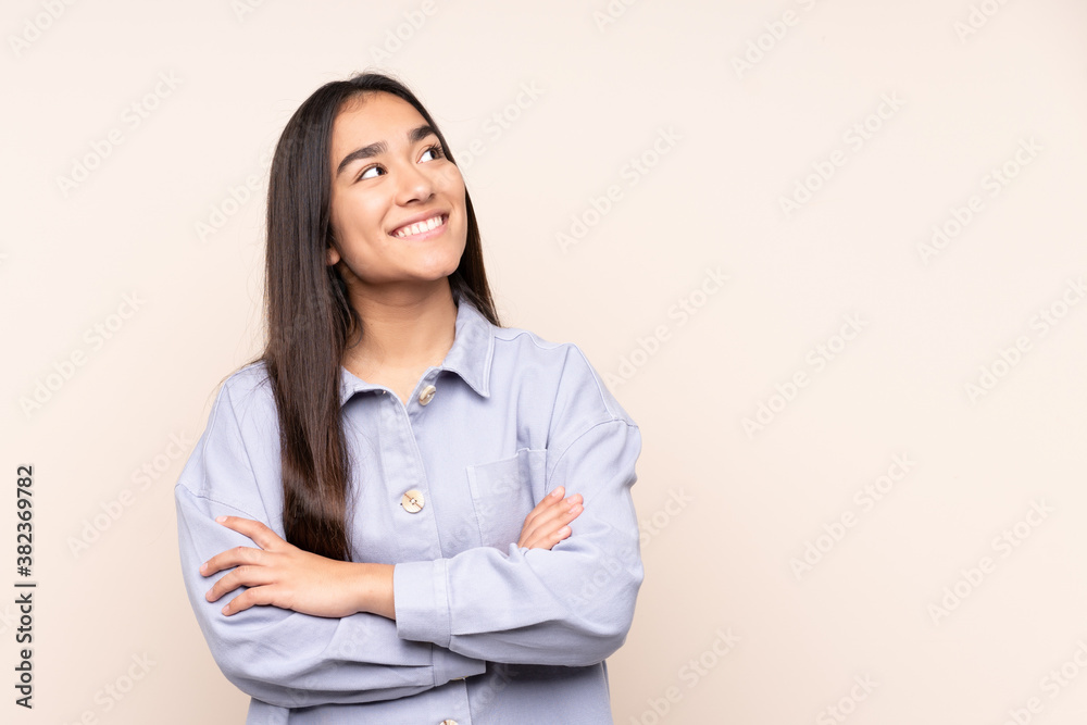 Young Indian woman isolated on beige background looking up while smiling Young Indian woman isolated on beige background looking up while smiling