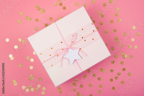 Top view of pastel pink gift box with bow and star with copy space on coral background decorated with golden confetti. Flat lay . Holiday festive concept. © greola84