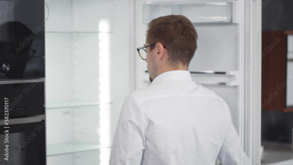 Hungry young man in glasses looking into empty refrigerator