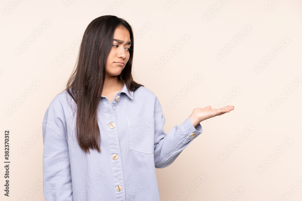 Young Indian woman isolated on beige background holding copyspace with doubts
