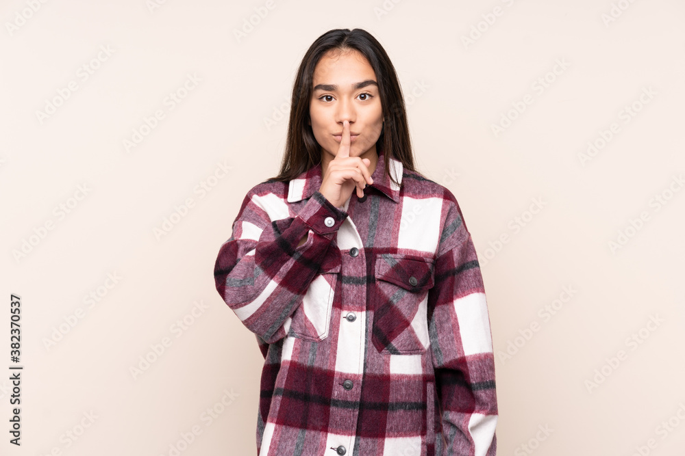Young Indian woman isolated on beige background showing a sign of silence gesture putting finger in mouth