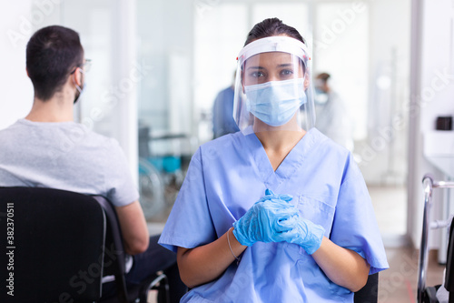 Bilde på lerret Nurse looking at camera wearing surgical face mask against coronavirus in hospital hallway as safety precaution