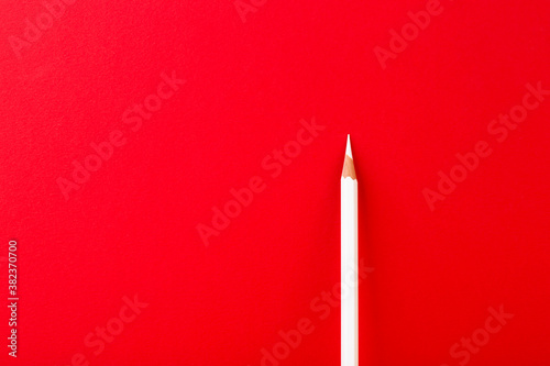 One lonely white pencil on deep red paper background