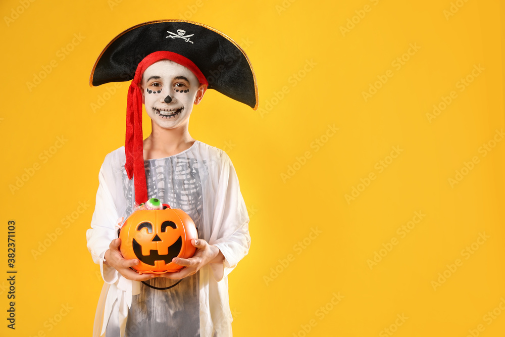 Cute little boy with pumpkin candy bucket wearing Halloween costume on yellow background. Space for text
