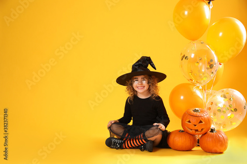 Fototapeta Cute little girl with pumpkins and balloons wearing Halloween costume on yellow background