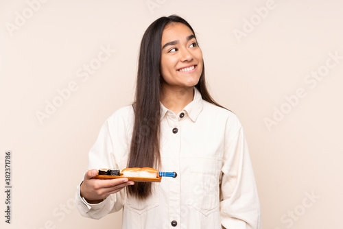 Young Indian woman holding sushi isolated on beige background looking up while smiling
